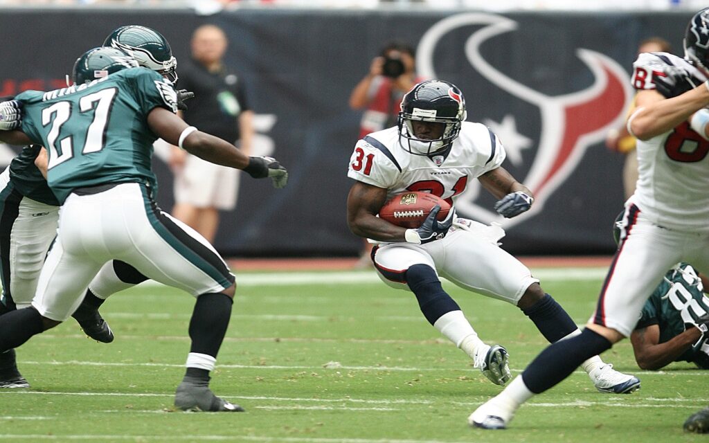 A football player sprinting with the ball, evading opponents in a dynamic on-field action scene.